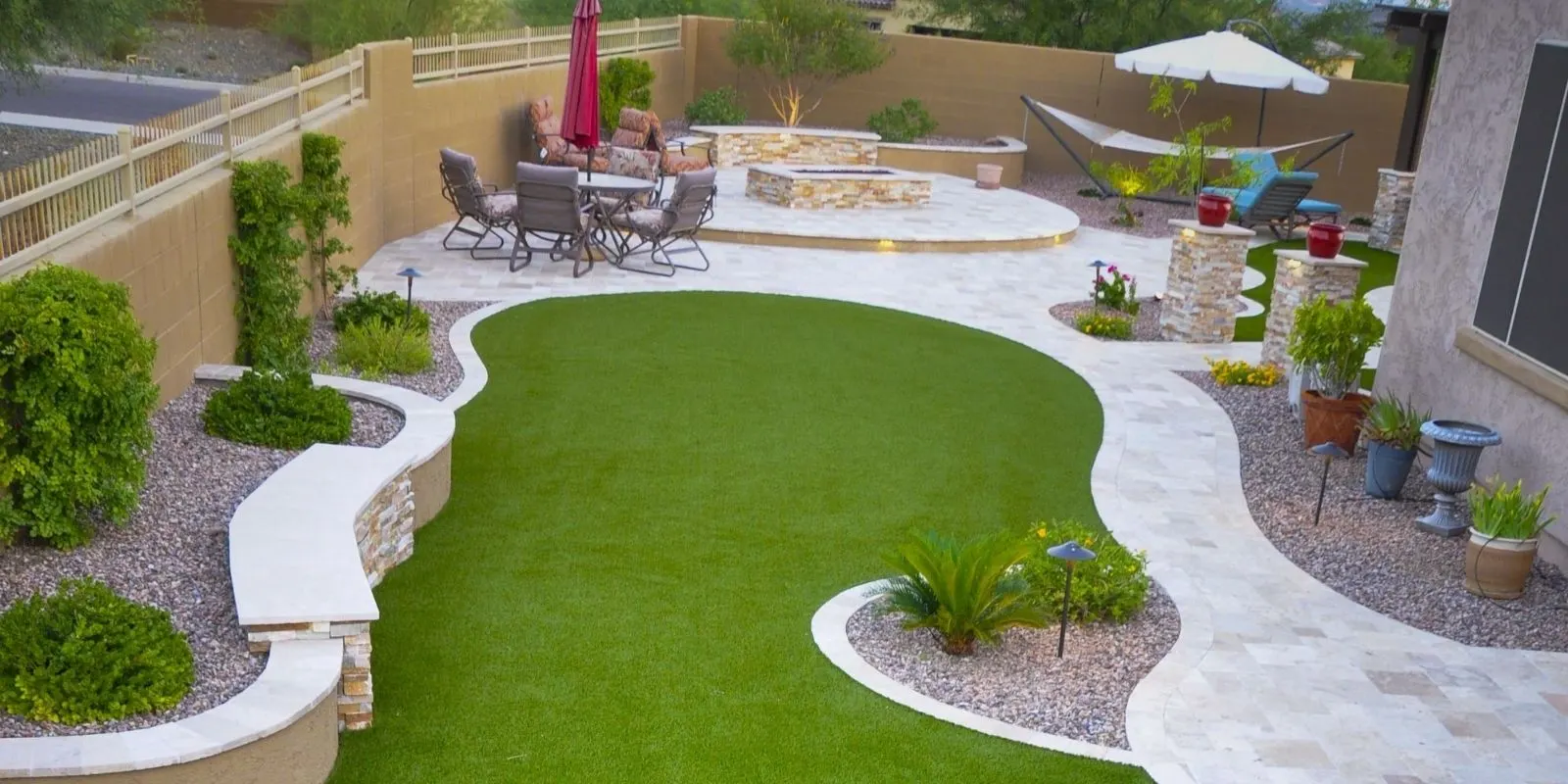 Curved backyard lawn of artificial turf bordered by stone pavers and gravel beds