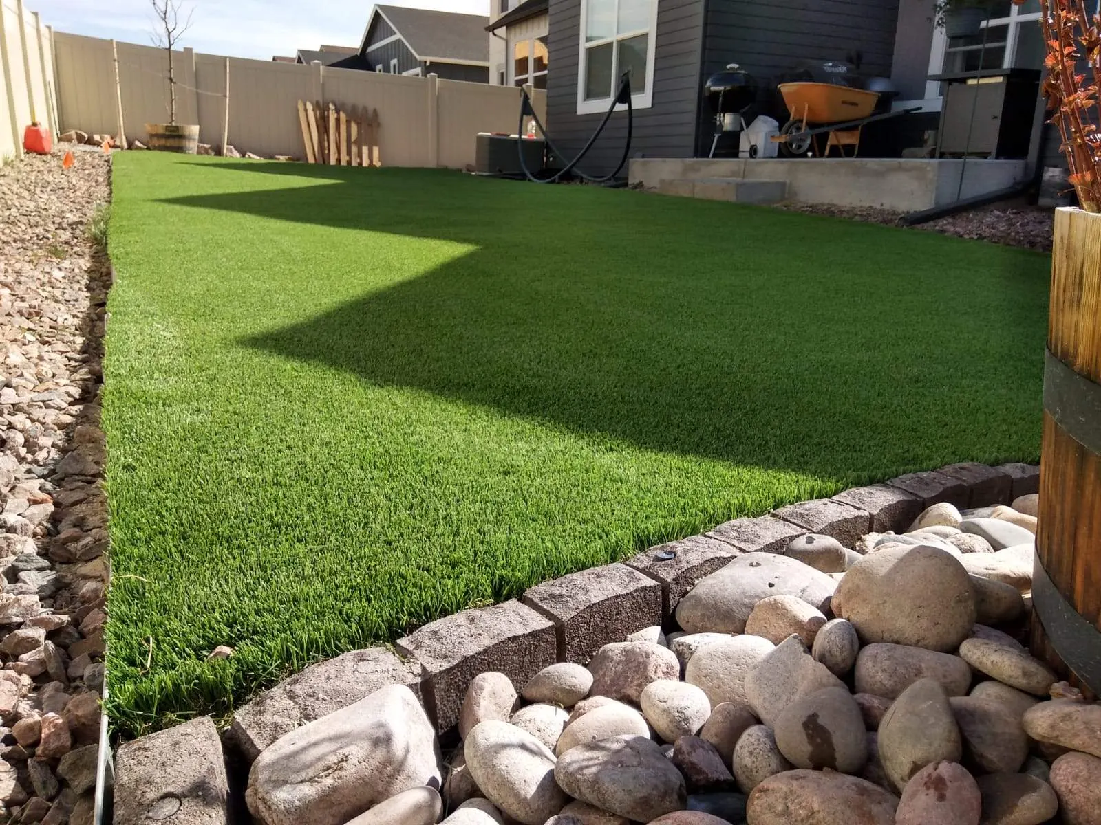 Backyard artificial lawn edged with block border and river rock