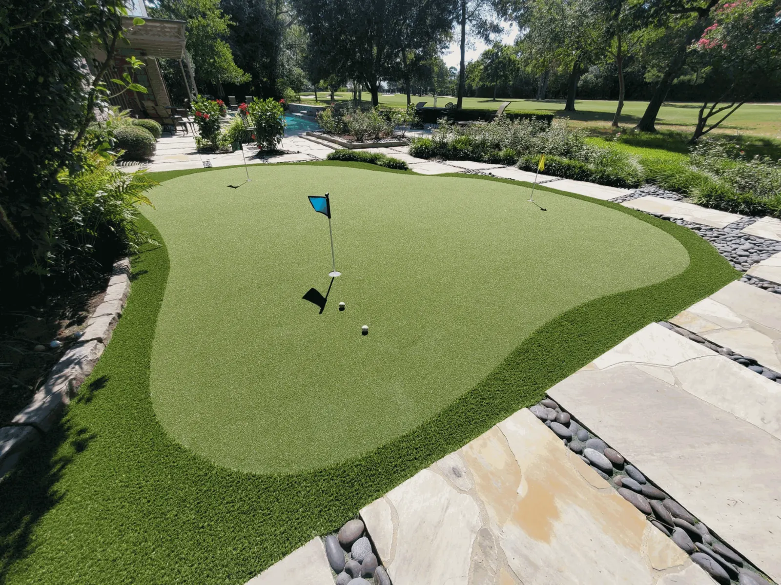 Backyard putting green with flags and fringe turf beside a flagstone walk