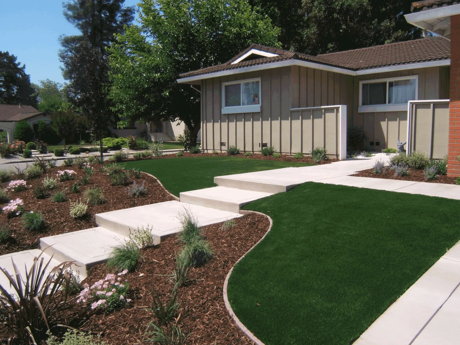 Artificial grass front lawn beside concrete steps and planted mulch beds