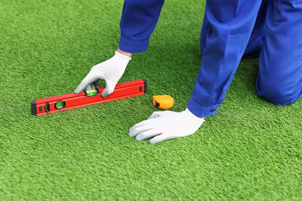 Installer in work gloves checking newly laid turf with a level
