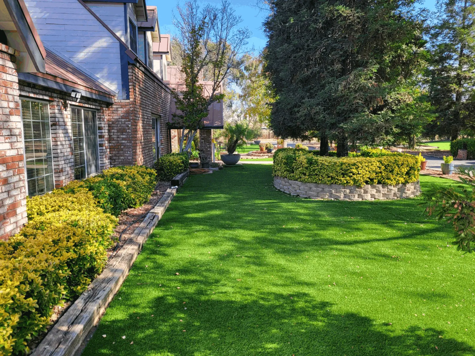 Artificial turf side lawn beside a brick house and a raised planter